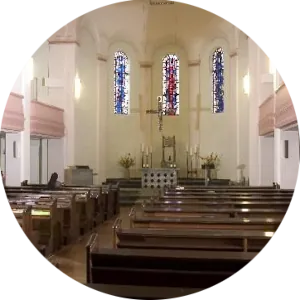 Kircheninnenraum mit Bänken und Buntglasfenstern.