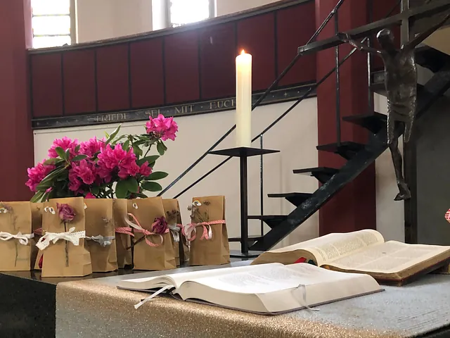 Altarbereich mit geöffneten Büchern, Kerze, Blumen und kleinen Geschenktüten.